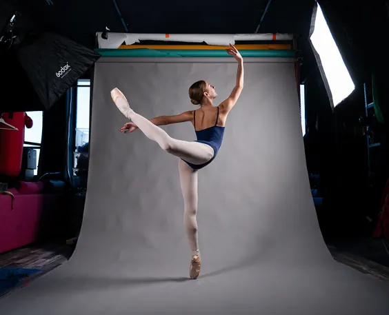 A ballet dancer in arabesque on a grey paper backdrop, lit by studio softboxes
