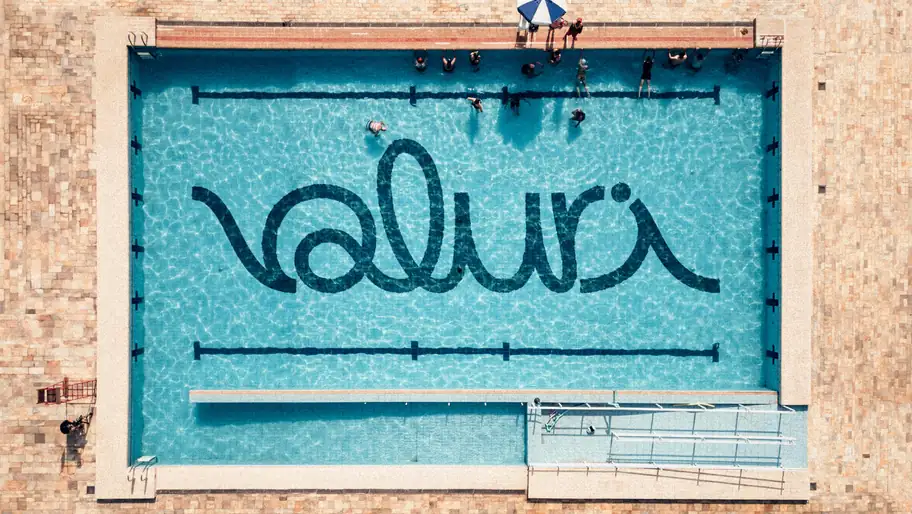 The Valuri logo laid in dark tiles on the floor of an outdoor pool, seen from above