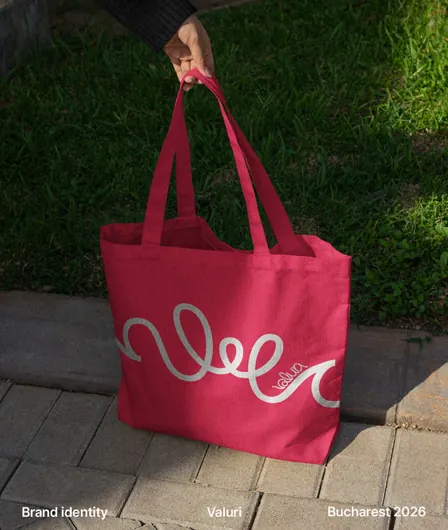 A red Valuri tote bag with the white wave line, held over the grass